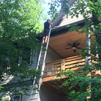 Man on tall ladder cleaning gutters on mountain home in forest