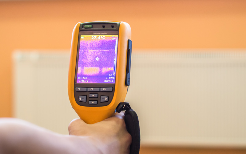 Photo of energy audit technician scanning a home with a thermal imaging device to identify heat leaks