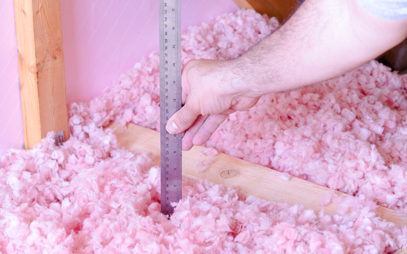 Photo of insulation contractor measuring blown-in fiberglass insulation