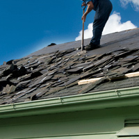 Man on roof removing existing shingles as part of a roof replacement project